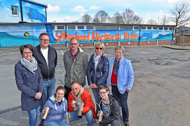 Offizielle Präsentation der mit Graffiti-Kunst verschönerten westlichen Fassade am Freibad der Gemeinde Wickede (Ruhr). Vordere Reihe, von links: Schülerin Lilli Knop, Grafitti-Künstler Patrick Sziedat aus Herne-Wanne und Schülerin Klara Dämgen mit Farbspraydosen. Hintere Reihe, von links: die Sponsoren-Vertreter Antje Kuss von der Sparkasse SoestWerl und Ralf Hettwer als Vorsitzender des Fördervereins des Freibades Wickede (Ruhr) sowie Schwimmmeister Michael Scheffler, die verantwortliche Sachbearbeiterin Ruth Hornkamp aus dem Rathaus und die stellvertretende Bürgermeisterin Gertrud Martin (CDU) von der Gemeinde Wickede (Ruhr). FOTO: ANDREAS DUNKER 