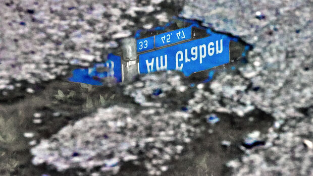 Die Straße "Am Graben" ist übersät von Schlaglöchern. Nach Niederschlägen spiegelt sich im Regenwasser der Pfützen das Straßenschild. FOTO: ANDREAS DUNKER